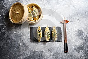 Boiled and hot chinese dumplings in wooden steamer and on black stone board slate over grey stone textured table background top