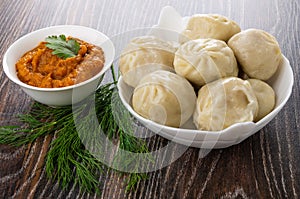 Boiled khinkali in bowl, dill, bowl with squash caviar on dark wooden table