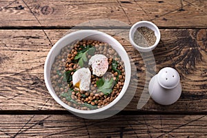 Boiled lentils with spinach, herbs, spices and poached egg in ceramic bowls on a wooden background