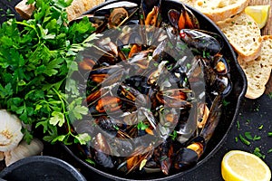 Boiled mussels in iron pan cooking dish. with herbs, butter, lime, parsley, garlic and fresh bread.