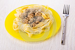 Boiled noodles with fried mincemeat in yellow plate, fork