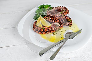 Boiled octopus with lemon ,parsley and salad dressing on white plate. Traditional mediterranean seafood