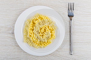 Boiled pasta fusilli in plate, fork on wooden table