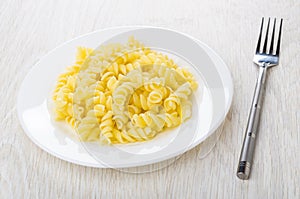 Boiled pasta fusilli in white plate and fork on table