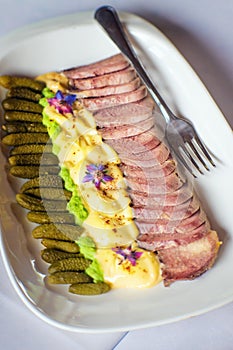 Boiled pork meat on a white plate with pickles and mayonnaise.