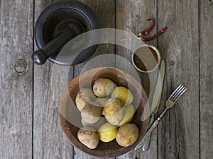 Boiled potatoes in their skins. whole with red pepper, salt and spicy sauce on clay plate, old wooden table, rustic