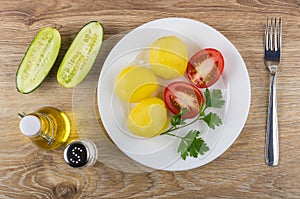 Boiled potatoes with tomato and parsley in plate, cucumbers, oil