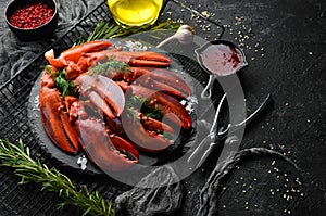 Boiled red lobster claws with spices and parsley on a black stone plate. On a black background.