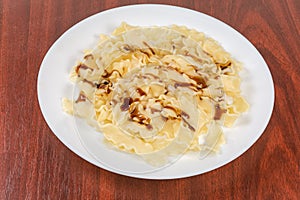 Boiled short noodles with sauce on dish on wooden table