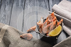 Boiled shrimps served with lemon in a small bowl over rustic wooden background with cloth