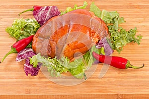 Boiled-smoked pork knuckle with lettuce leaves on cutting board