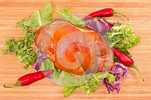 Boiled-smoked pork knuckle with lettuce leaves on cutting board