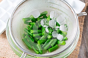 Boiled vegetables, green beans in a colander in ice water after blanching