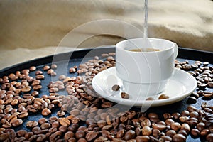 Boiled water is poured into a white cup with black coffee. Roasted coffee beans