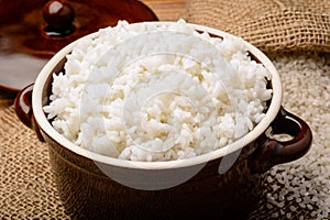 Boiled white rice in ceramic pot on wooden background.