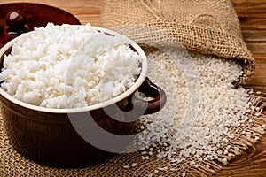 Boiled white rice in ceramic pot on wooden background.