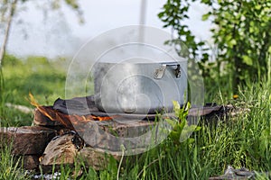 Boiler with steam stands on open fire. The concept of cooking on campsite