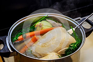 Boiling chicken broth with vegetables in steel pot on gas stove top