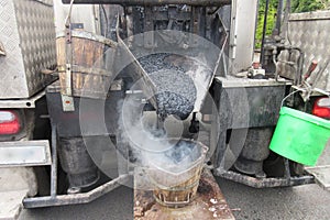 Boiling hot asphalt is filled into a bucket from an asphalt machine to fill a pothole. Road construction, road rehabilitation, as