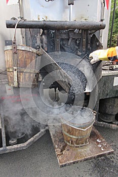 Boiling hot asphalt is filled into a bucket from an asphalt machine to fill a pothole. Road construction, road rehabilitation, as
