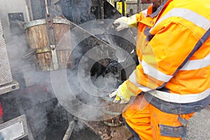 Boiling hot asphalt is filled into a bucket from an asphalt machine to fill a pothole. Road construction, road rehabilitation, asp