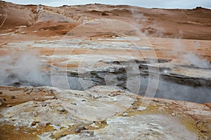 Boiling mudpots in the geothermal area Hverir and cracked ground around with unrecognisable tourists, Iceland in summer. Myvatn