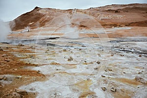 Boiling mudpots in the geothermal area Hverir and cracked ground around with unrecognisable tourists, Iceland in summer. Myvatn