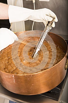 Boiling syrup of sugar in copper pan with thermometer and big spoon. Brown colour because of evaporation.