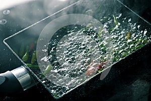 Boiling water with chili pepper in pan on electric stove in kitchen, hot water with bubbles and steam