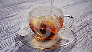 Boiling water is poured into a glass transparent cup with a bag of black aromatic tea