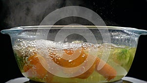 Boiling water with steam, cooking vegetables in glass pan