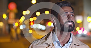 Bokeh shot of handsome man listening to music in earphones and singing outdoors