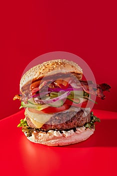 Bold fresh cheeseburger loaded with lettuce, cucumber, tomato and bacon on vibrant red