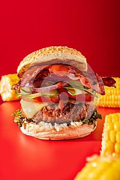 Bold fresh cheeseburger loaded with lettuce, cucumber, tomato and bacon on vibrant red