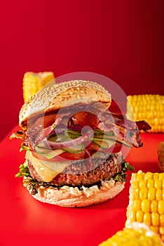 Bold fresh cheeseburger loaded with lettuce, cucumber, tomato and bacon on vibrant red