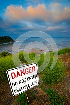 A bold sign warns visitors about the danger of an unstable cliff.