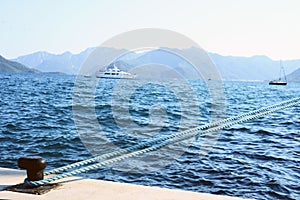 Bollard roped tied on the dock of blue sea water