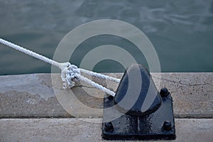 A bollard with a white rope tied to it from a harbour photo