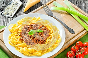 Bolognese ragout with italian pasta on a white plate, decorated with basil leaves, authentic recipe, wooden background with celery