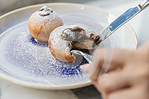 Bombolone is an Italian filled doughnut and is eaten as a snack food and dessert with hands cutting