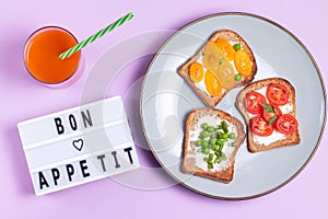 Bon appetite lettering on purple background with plate of vegetable sandwiches