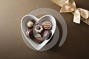Bonbons in ceramic heart-shaped on brown with golden gift bow