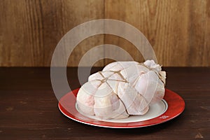 Bondage shibari raw chicken on red boarder plate on dark wood ba