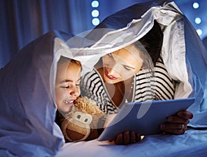 Bonding at bedtime. an attractive young pregnant woman reading her daughter a bedtime story on a tablet.