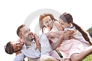 Bonding. Family of four sitting on a grassy field hugging smilin