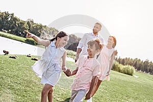 Bonding. Family of four walking on a grassy field near lake kids