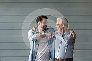 Bonding mature grandpa young grandson bump fists by grey wall
