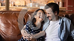 Bonding young spouses laugh hug on couch in playful mood