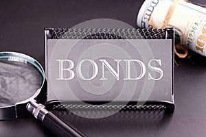 BONDS text on the business card next to the money, a magnifying glass on a black background