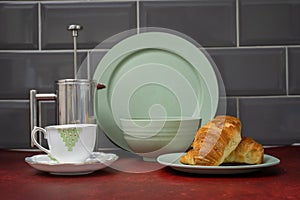 bone china coffee cup and saucer stainless steel cafetiere with fresh coissant green dinner set on red linoleum work top with